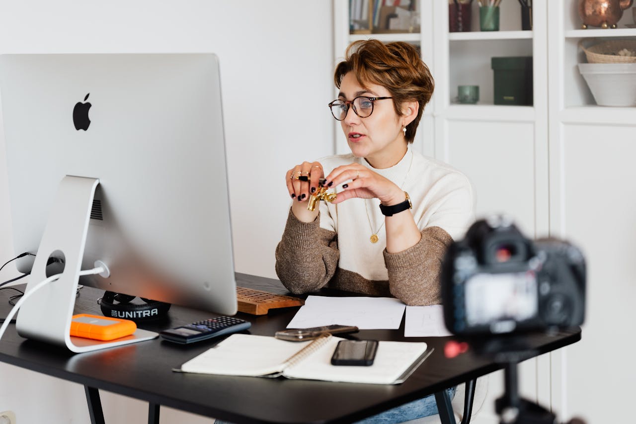 services-01 A professional woman engaged in a virtual meeting setup at her home desk, using a computer and camera.